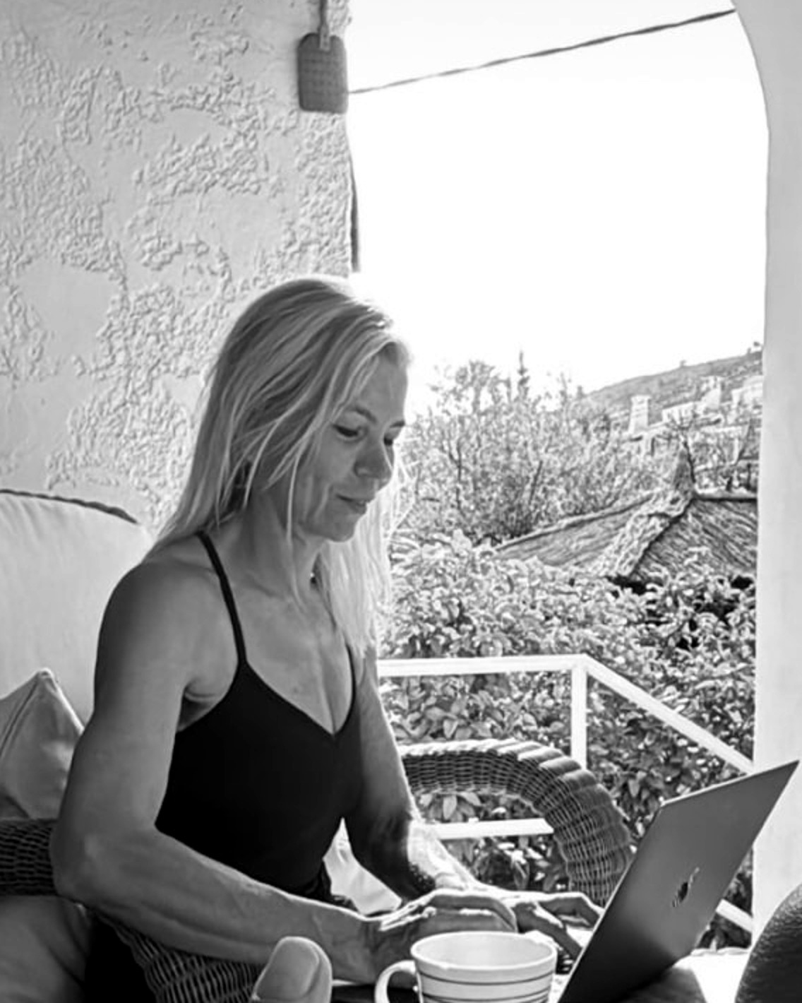 Black and white photo of Cecilia Tibell writing on a sunlit terrace in Spain